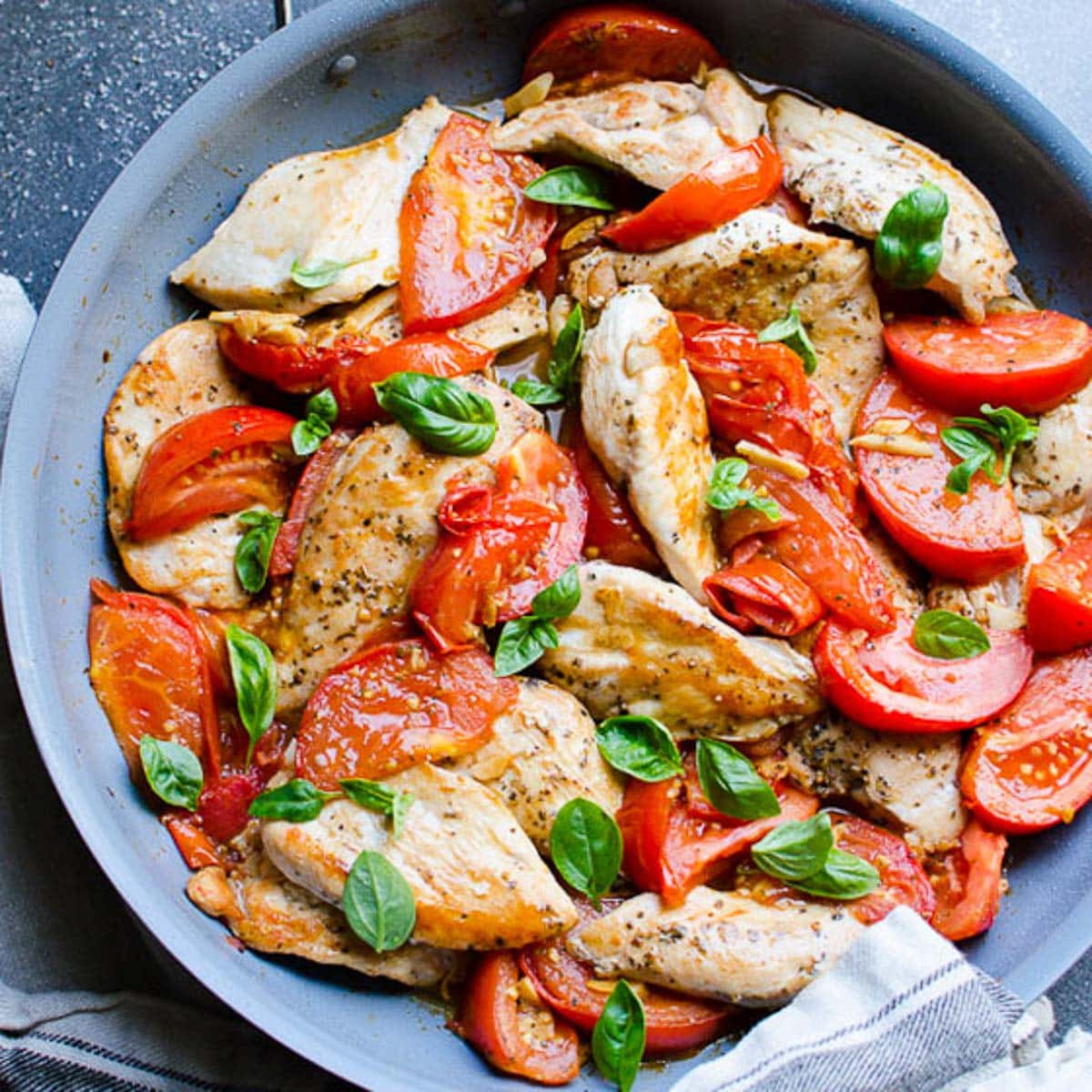 Chicken with tomatoes and garlic in a skillet garnished with basil.