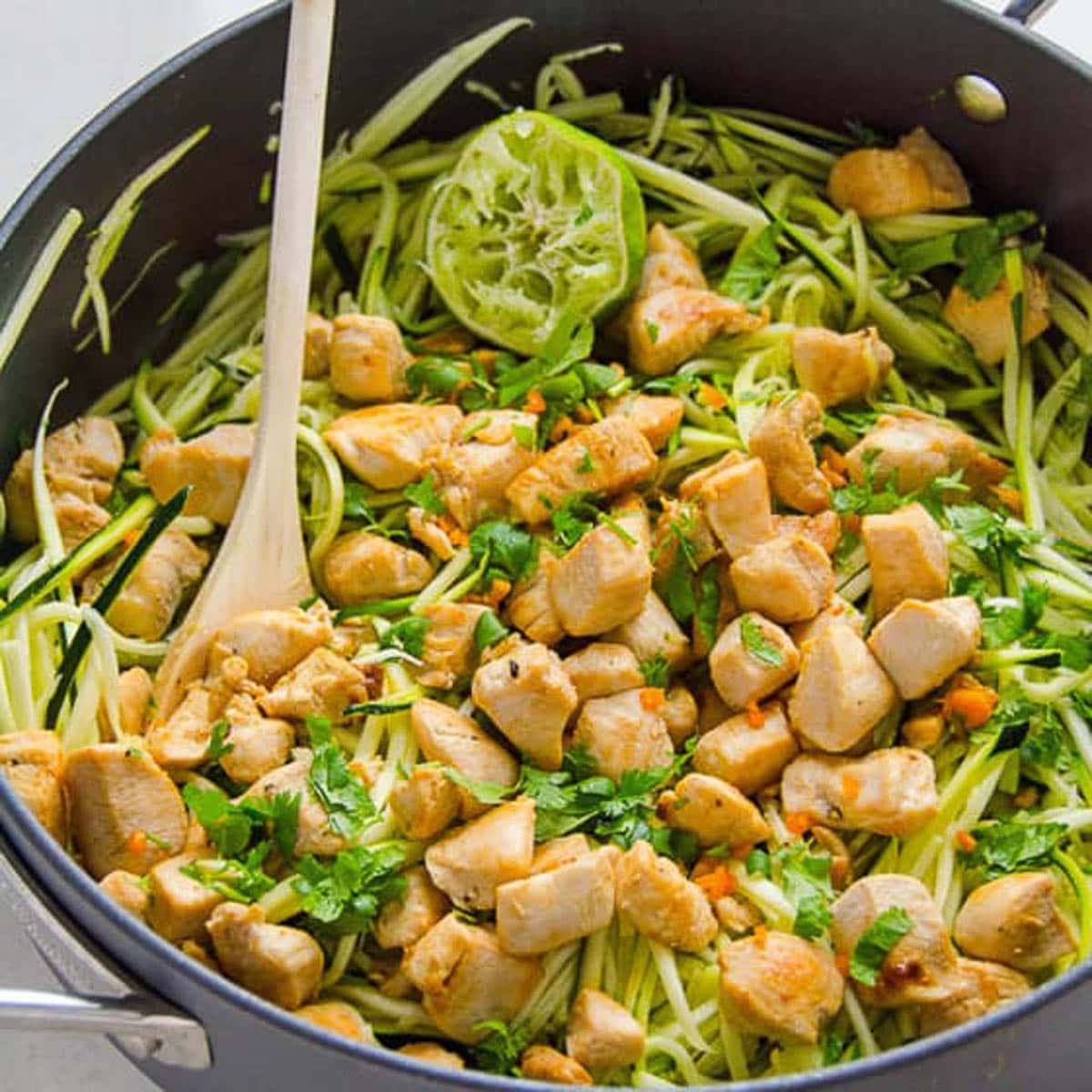 Zucchini noodles with cilantro and lime chicken in black skillet with wooden spoon.