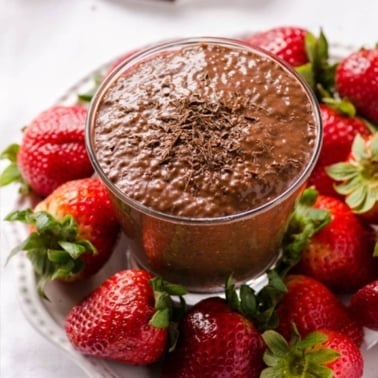 Chocolate chia pudding in a glass on a plate with fresh strawberries.