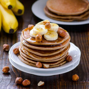A stack of cottage cheese protein pancakes topped with sliced bananas and hazelnuts.