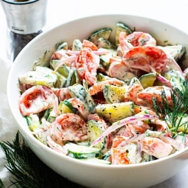 Creamy cucumber tomato salad in a bowl with sprig of fresh dill.