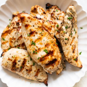 Grilled chicken breasts garnished with parsley and served on a plate.