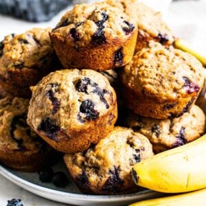 A plate of healthy blueberry banana muffins with fresh bananas.