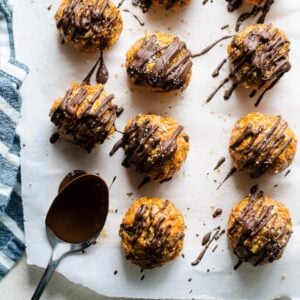 Carrot cake truffles drizzled with chocolate on parchment paper and spoon nearby.
