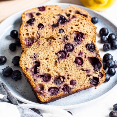Two slices of lemon blueberry bread on a plate with fresh berries.
