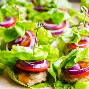 Turkey sliders with sliced tomato and red onion wrapped in lettuce.