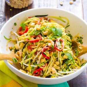 Pad Thai zucchini noodles salad in white bowl, linen napkin and peanuts nearby.