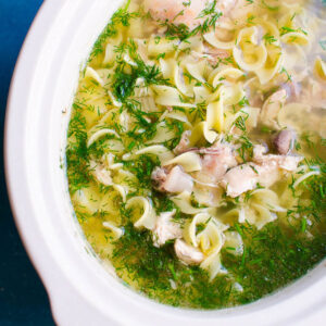 Slow cooker chicken noodle soup garnished with dill.
