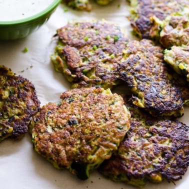 Tuna zucchini fritters served with dipping sauce and garnished with chives on parchment paper.