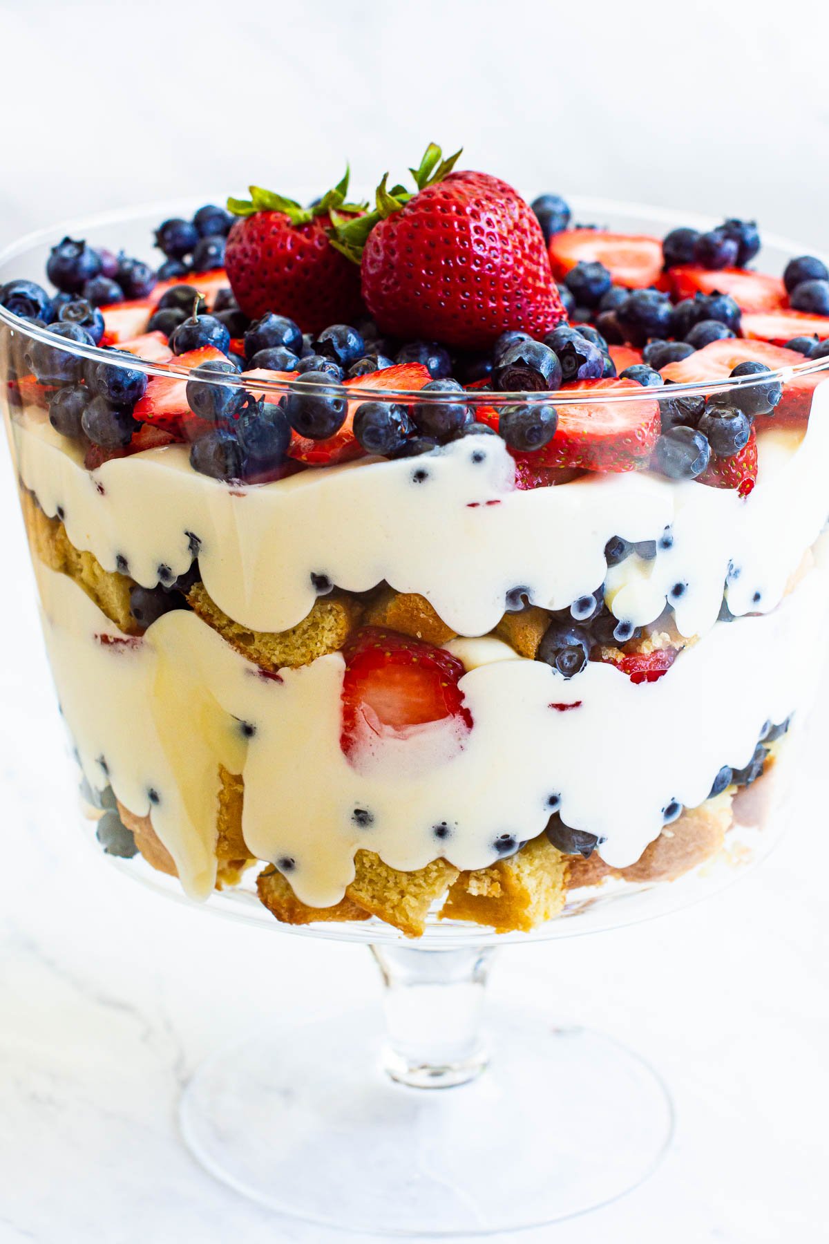 Cake, cream, blueberries and strawberries layered in glass trifle bowl.