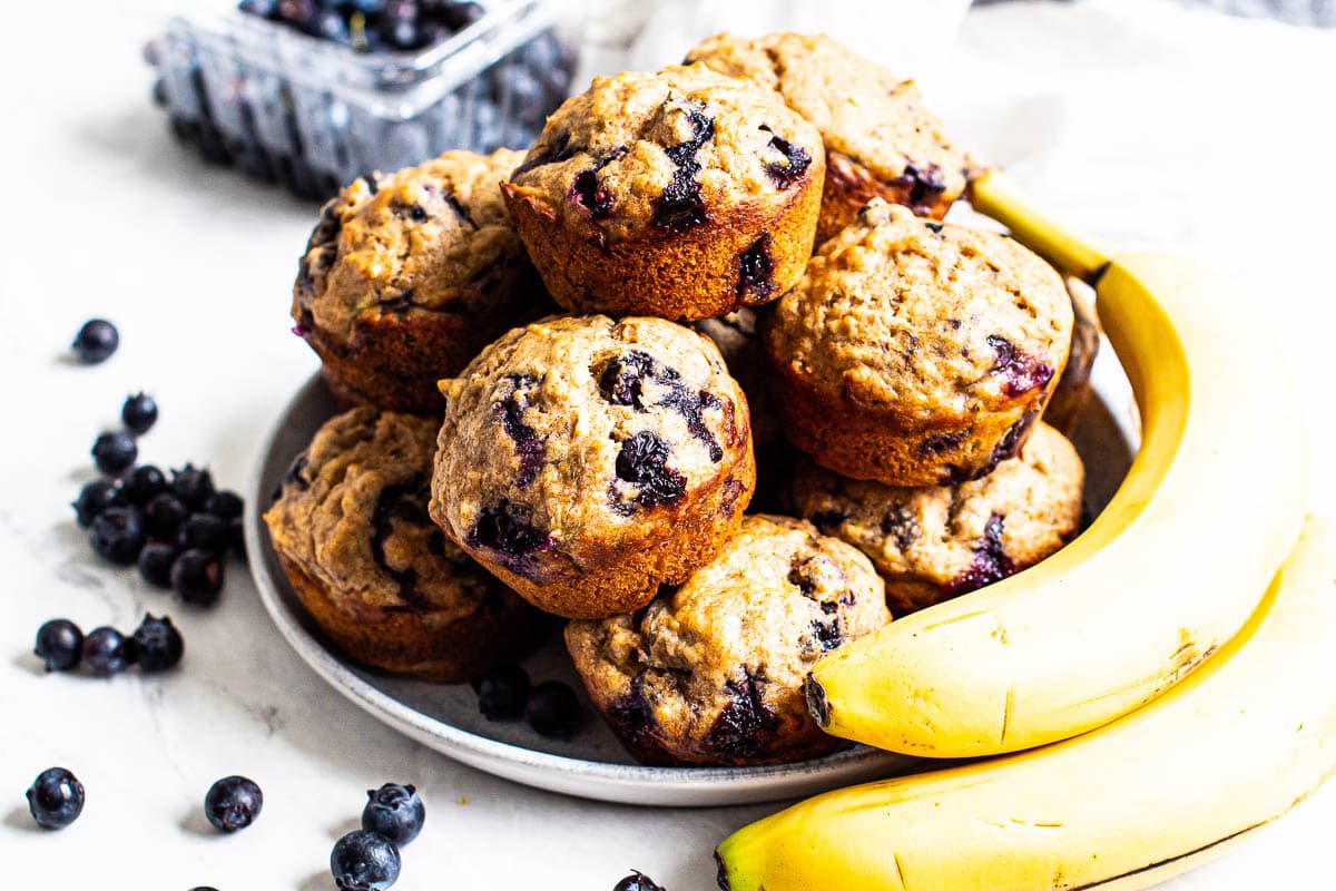 A plate of healthy blueberry banana muffins with fresh banana and berries.