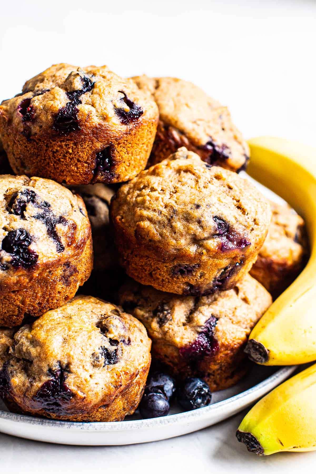 Healthy blueberry banana muffins stacked on a plate with some bananas.