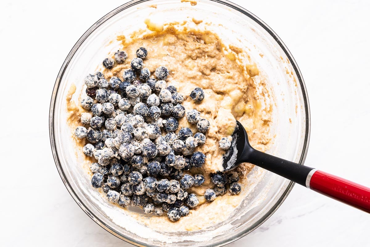 Blueberries tossed with flour in a bowl of muffin batter.