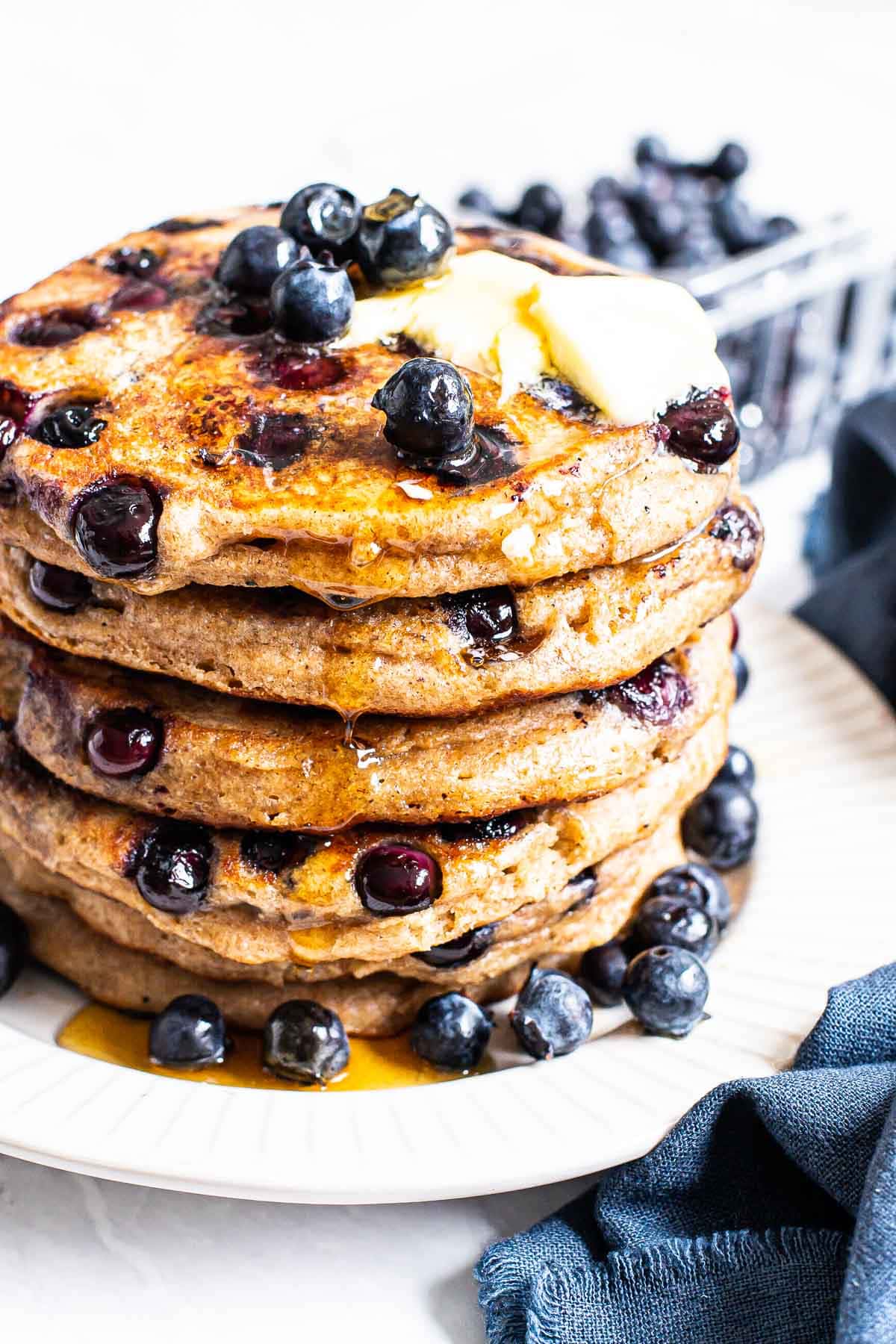 Healthy blueberry pancakes on a plate garnished with butter, maple syrup and blueberries.