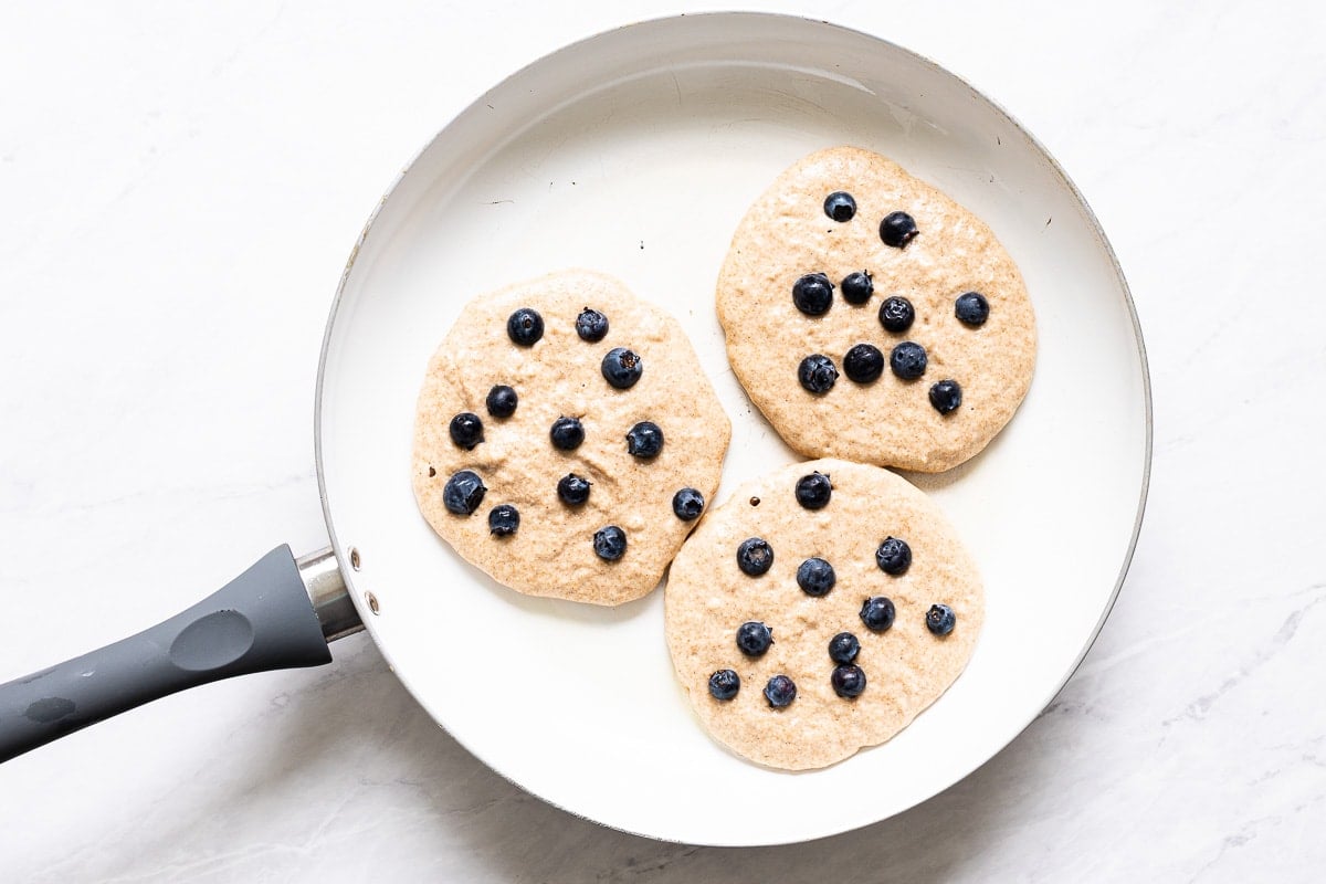 Three pancakes with blueberries in large skillet.