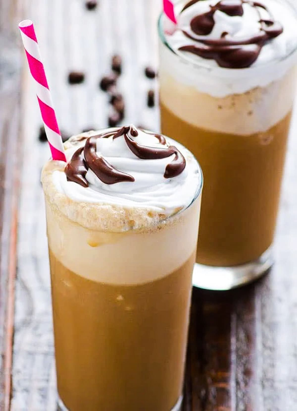 Healthy homemade frappuccino in two glasses with whipped topping, chocolate syrup and straws.