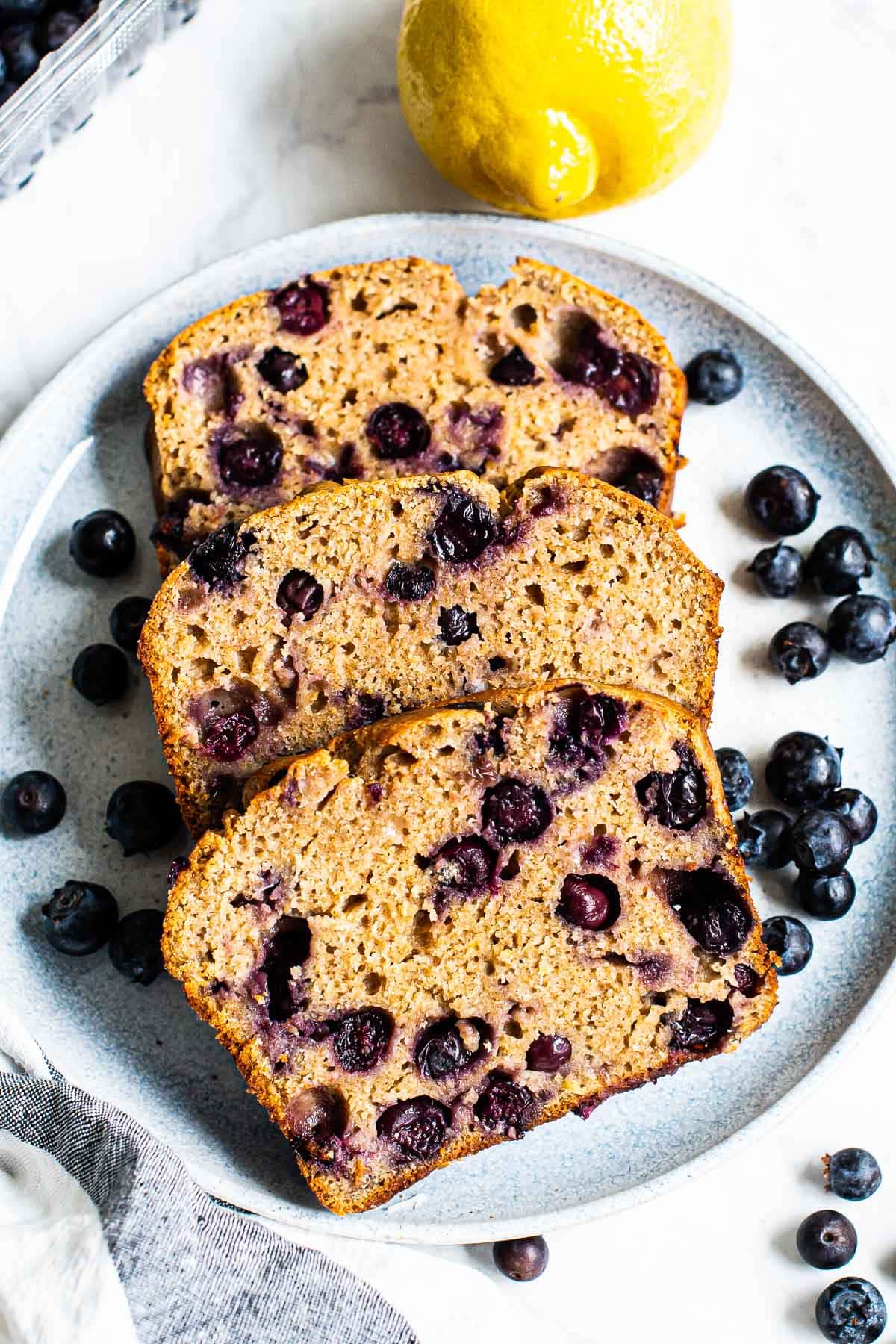 Three slices of healthy lemon blueberry bread on a plate garnished with blueberries.