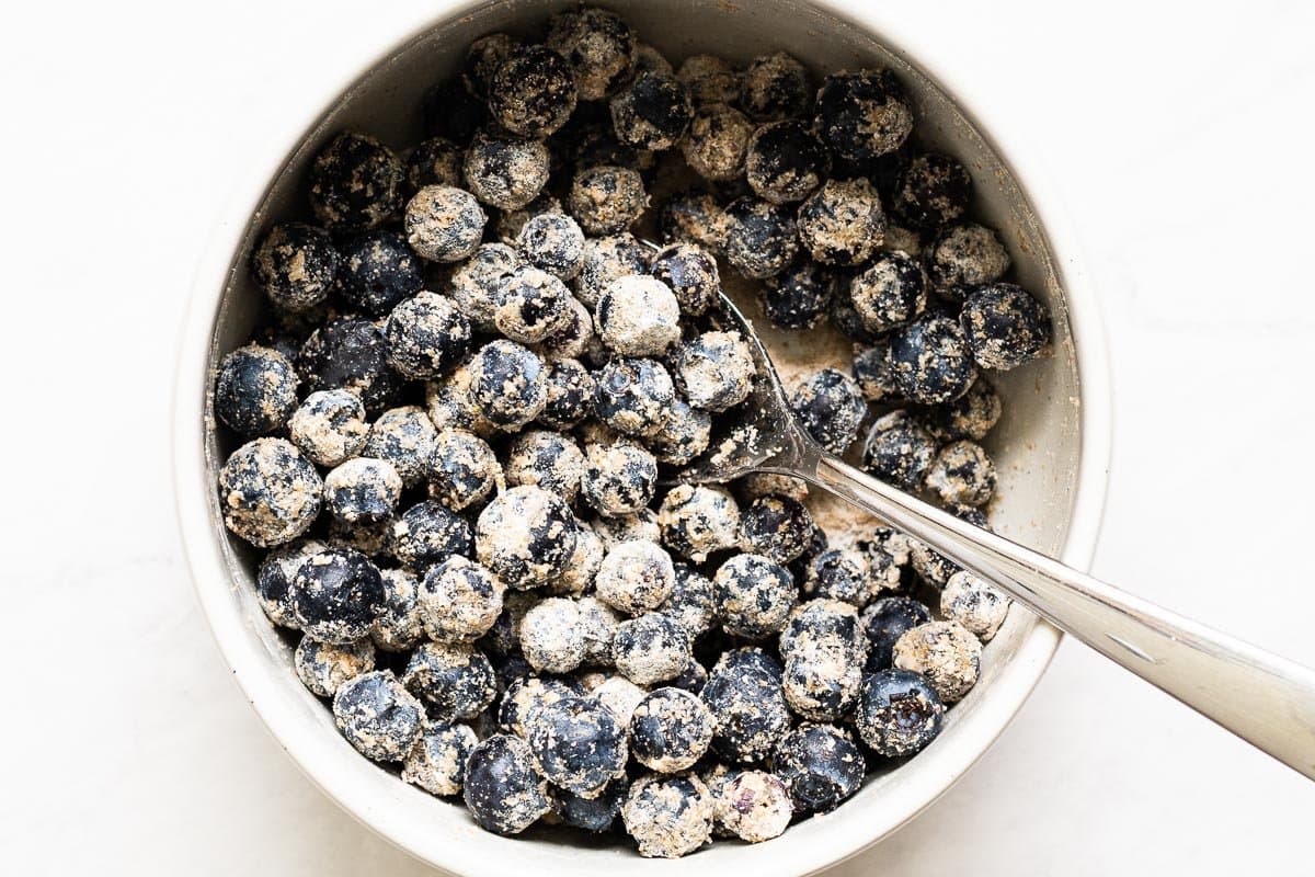 Blueberries coated in flour in a bowl with spoon.
