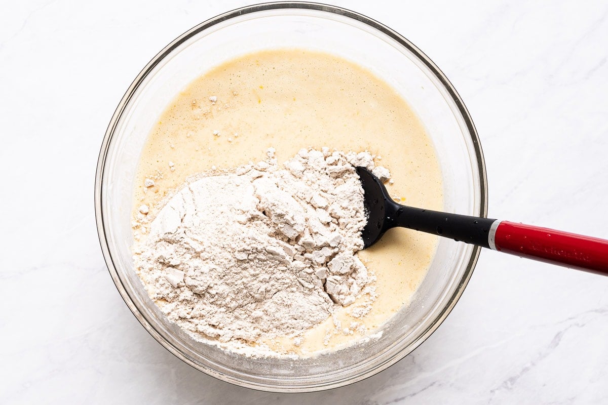 Adding flour to a bowl of liquid ingredients.