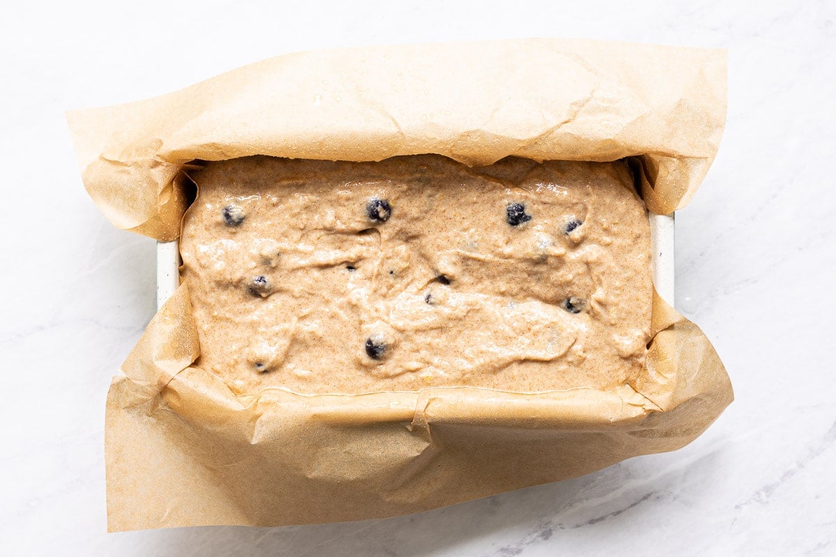 Quick bread batter with blueberries in parchment lined loaf pan.