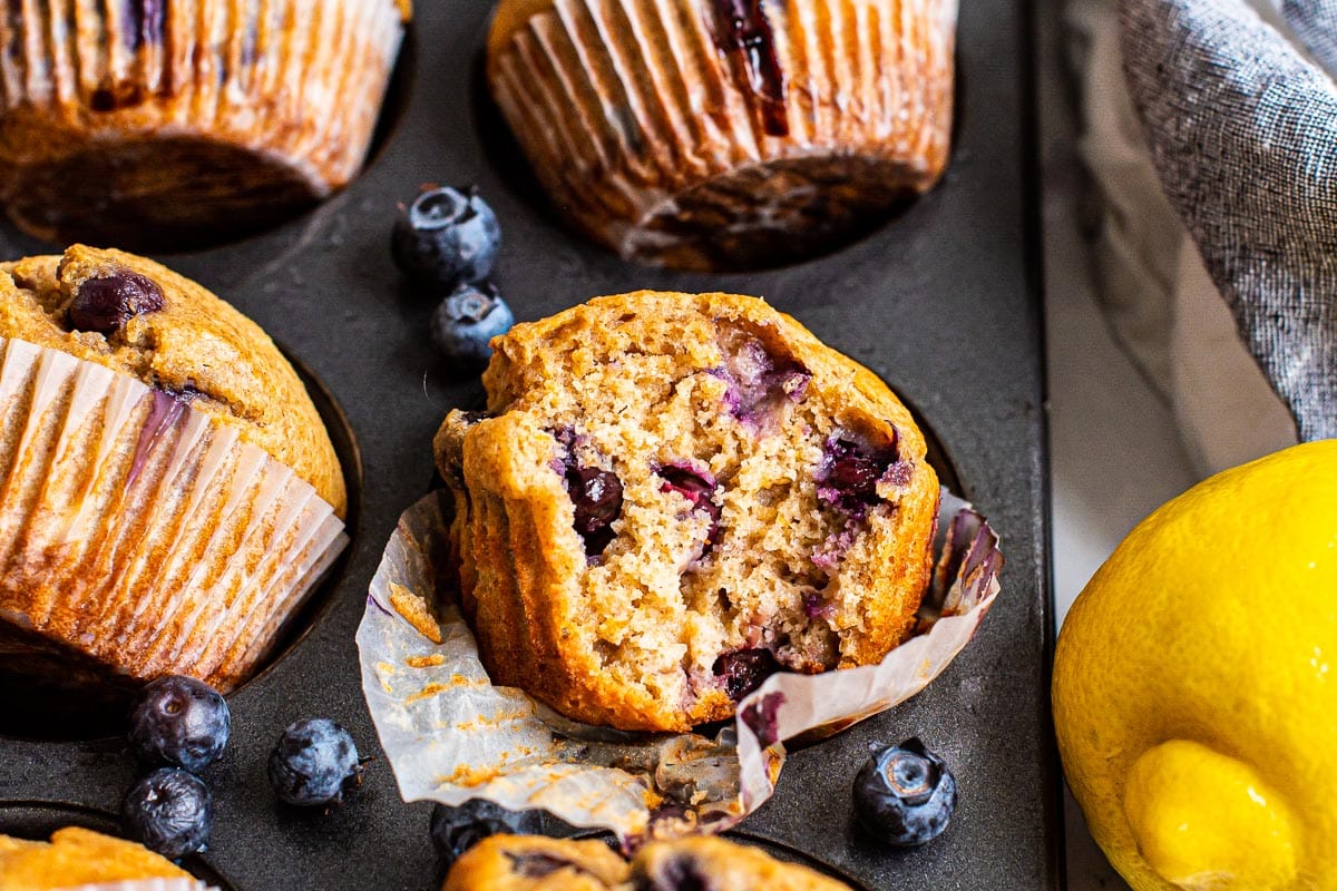 Healthy lemon blueberry muffins with one unwrapped a bite missing.