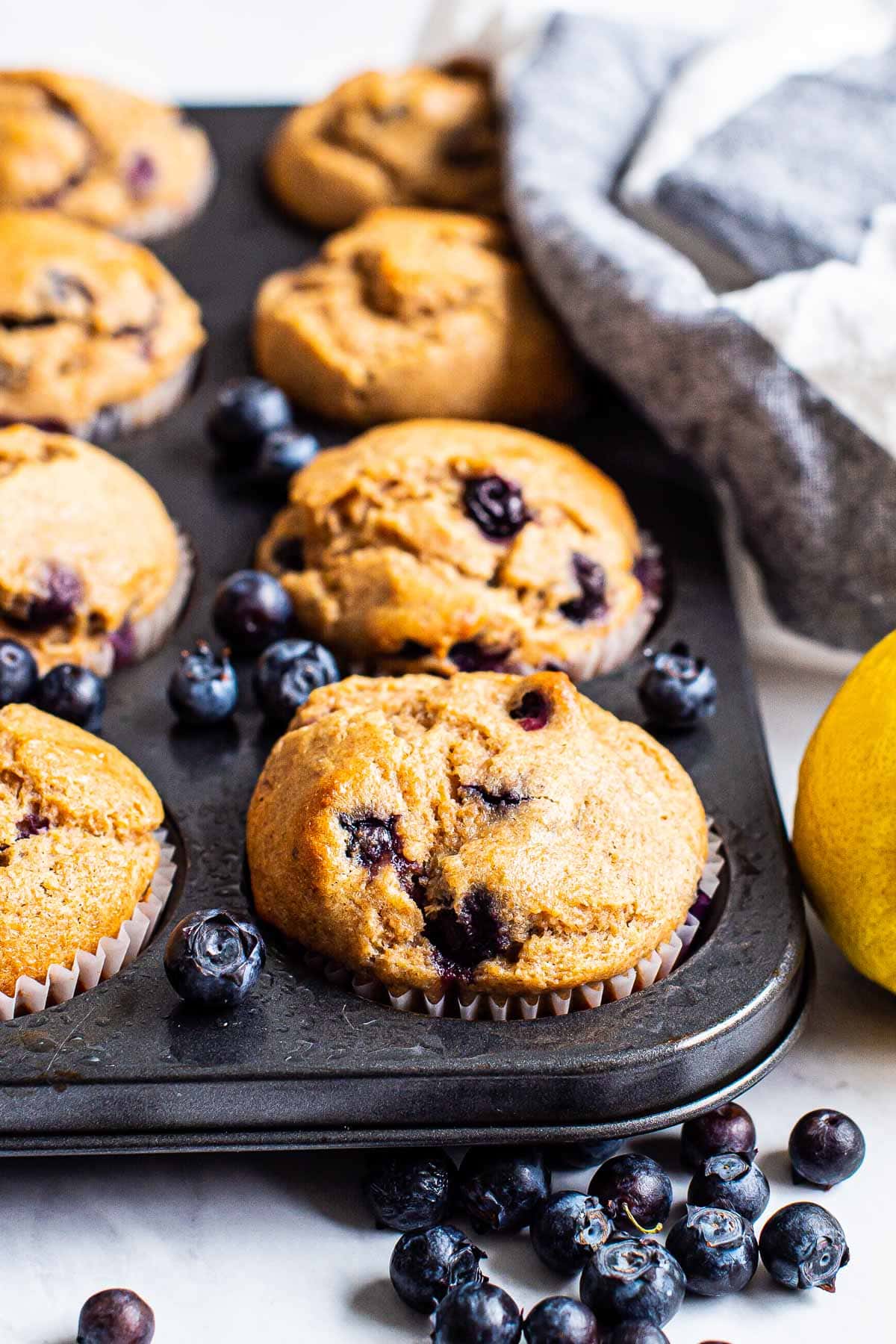 Healthy lemon blueberry muffins in a muffin tin with fresh blueberries.
