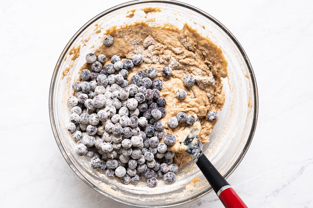 Flour dusted blueberries added to a bowl of batter.