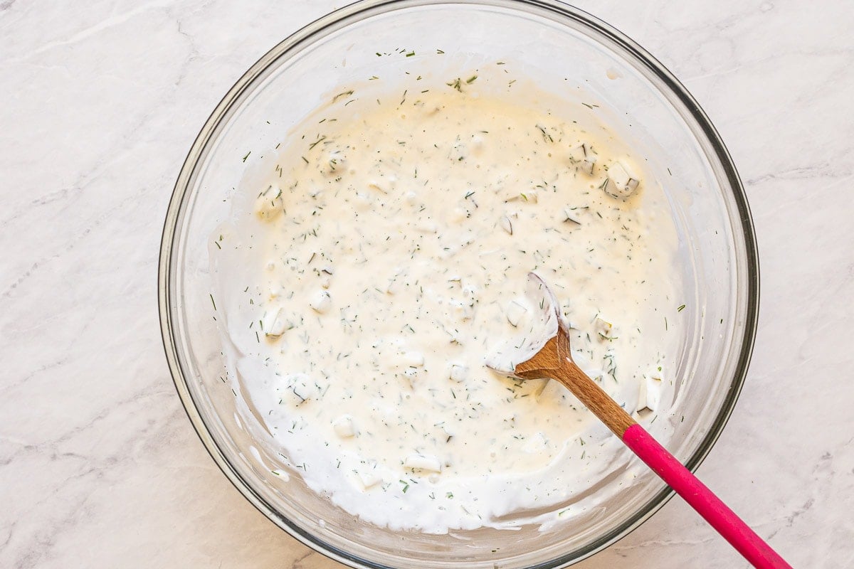 Creamy salad dressing in a bowl with a wooden spoon.