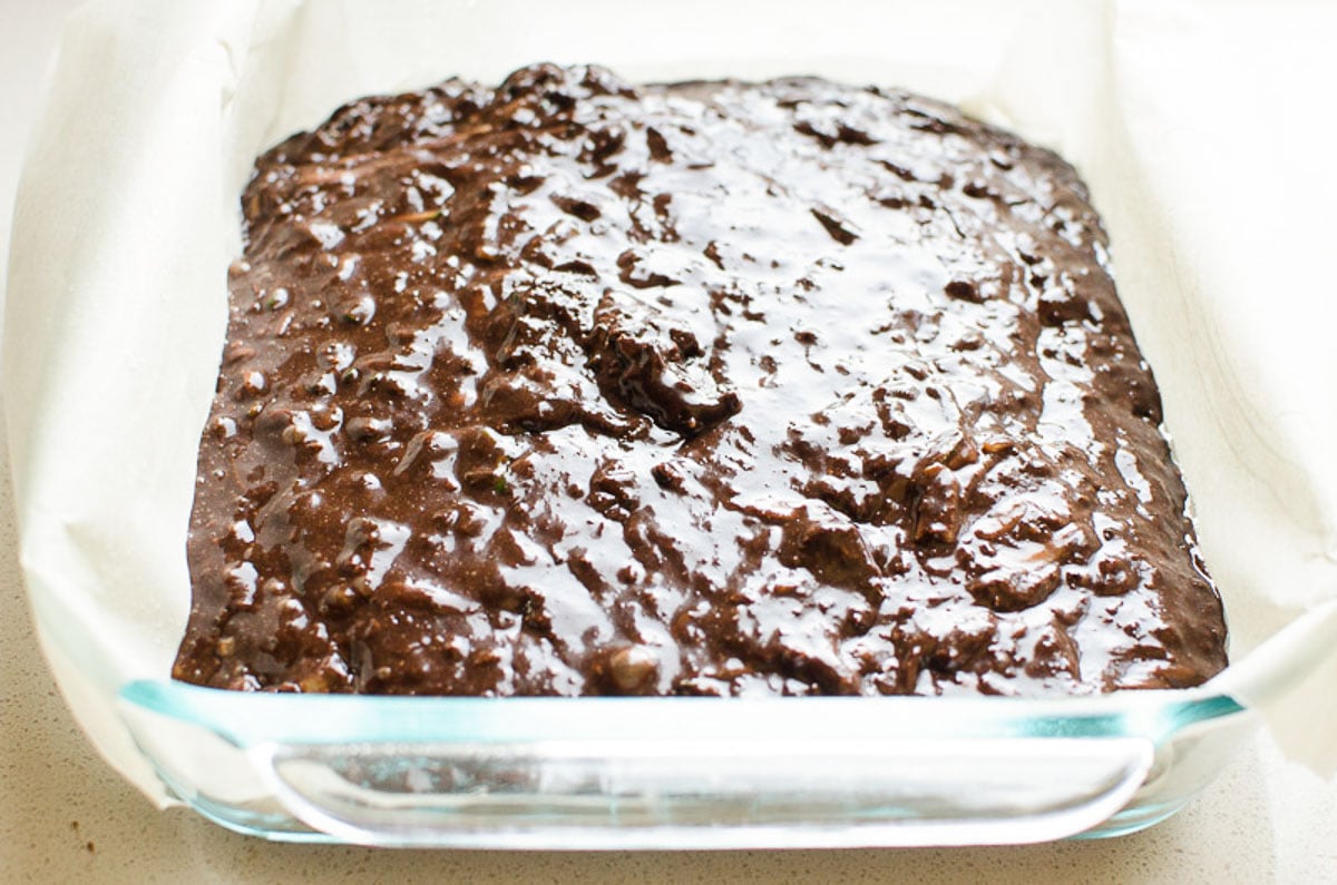 Healthy zucchini brownie batter in a baking dish lined with parchment paper.