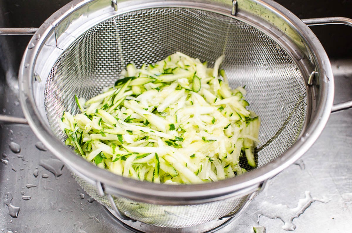 Shredded zucchini in a colander placed in a sink.