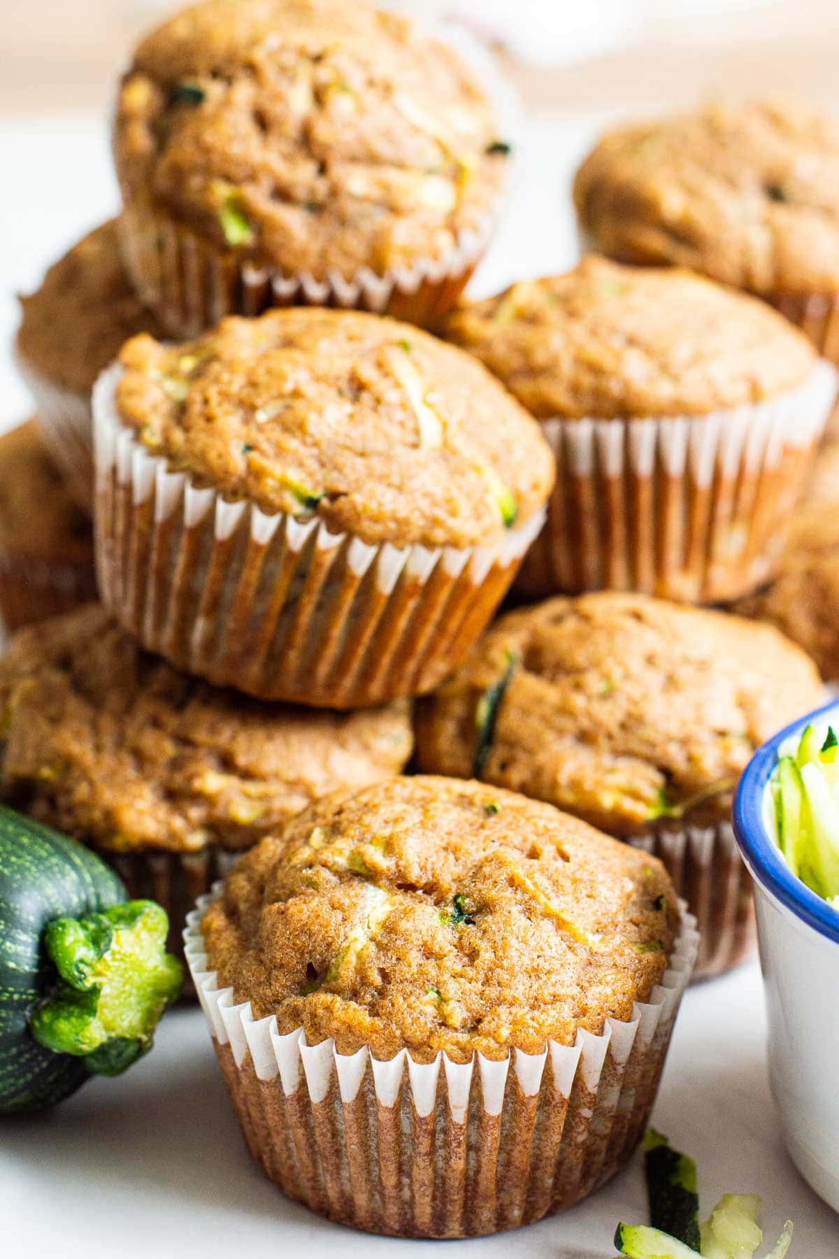 Healthy zucchini muffins in paper liners stacked on top of each other, fresh zucchini.