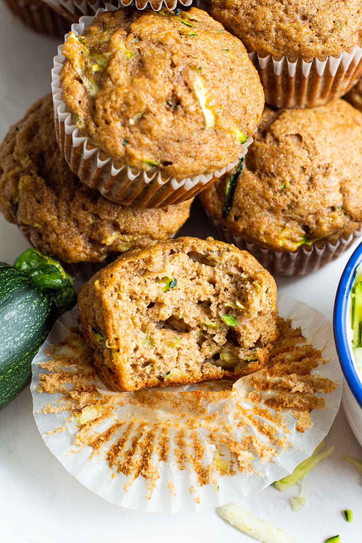 Five zucchini muffins with one unwrapped with a bite missing.