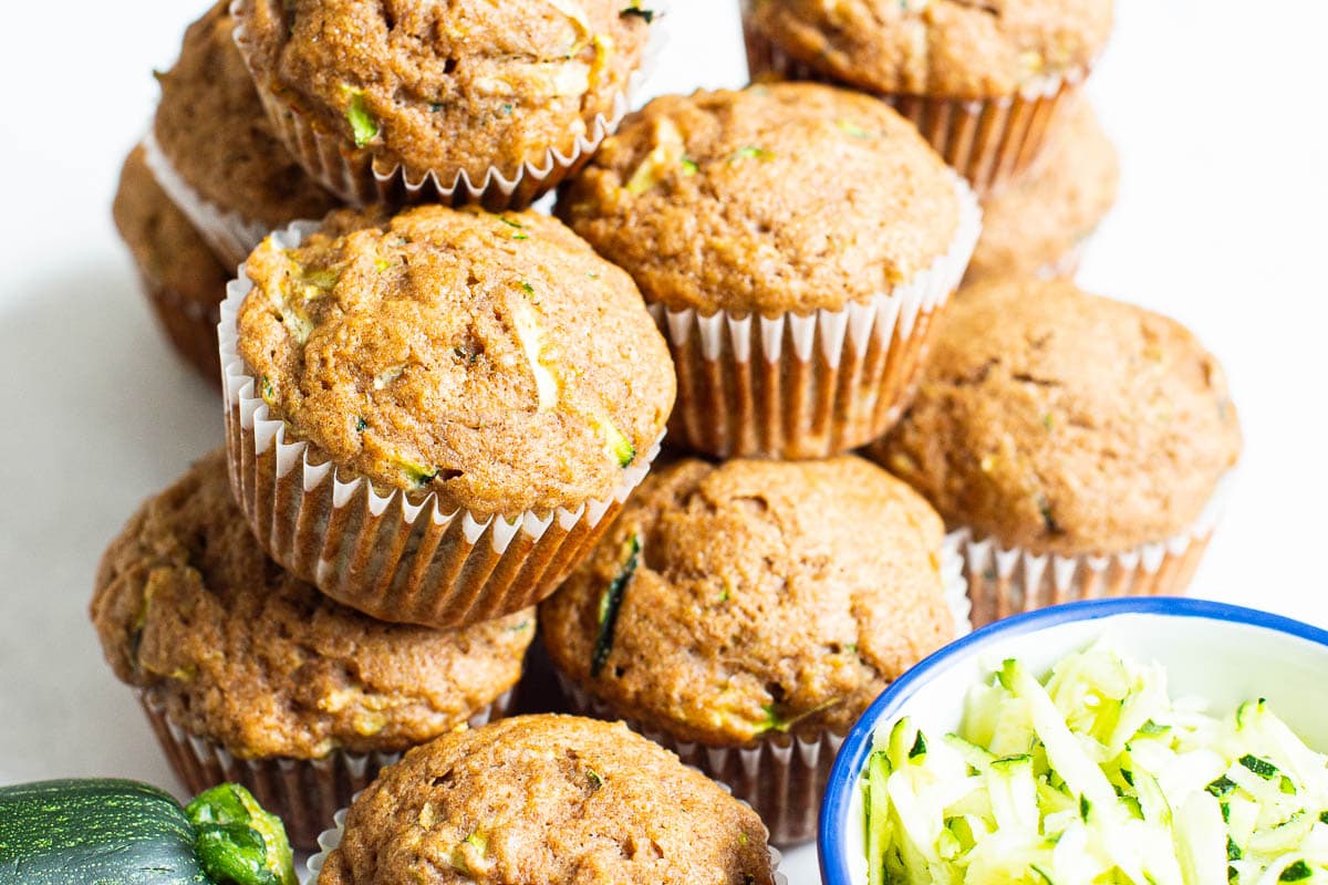 Healthy zucchini muffins with a bowl of shredded zucchini nearby.