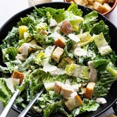 Healthy caesar salad in a bowl with serving spoons.