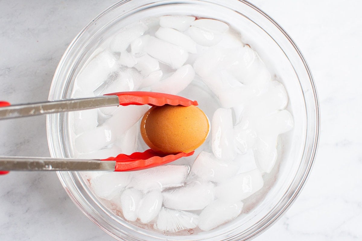 Transfering cooked egg with tongs into an ice bath.