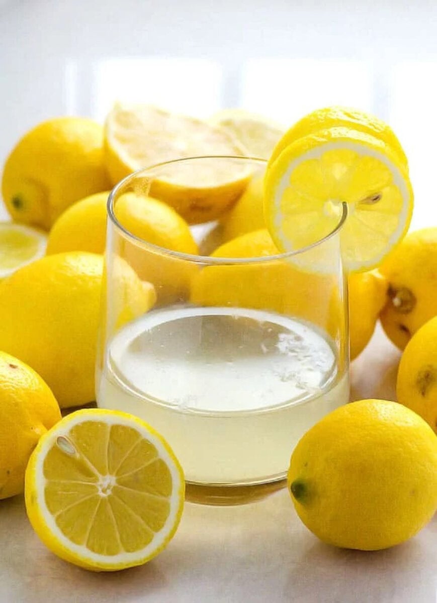 Lemon water in a glass surrounded by lemons.
