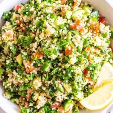 Quinoa tabbouleh salad in white bowl with lemon slices.