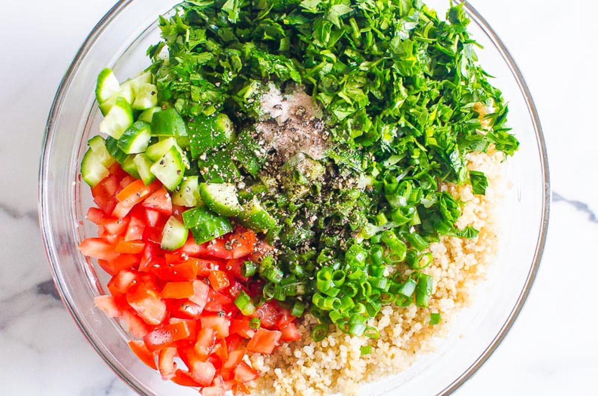 Fresh parsley, mint, cooked quinoa, cucumbers, green onions, tomatoes and seasonings in bowl.