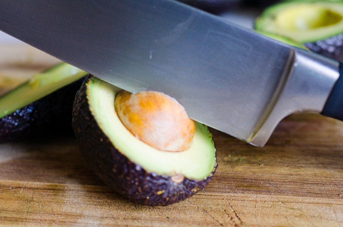 Chef's knife in a pit of half sliced avocado.
