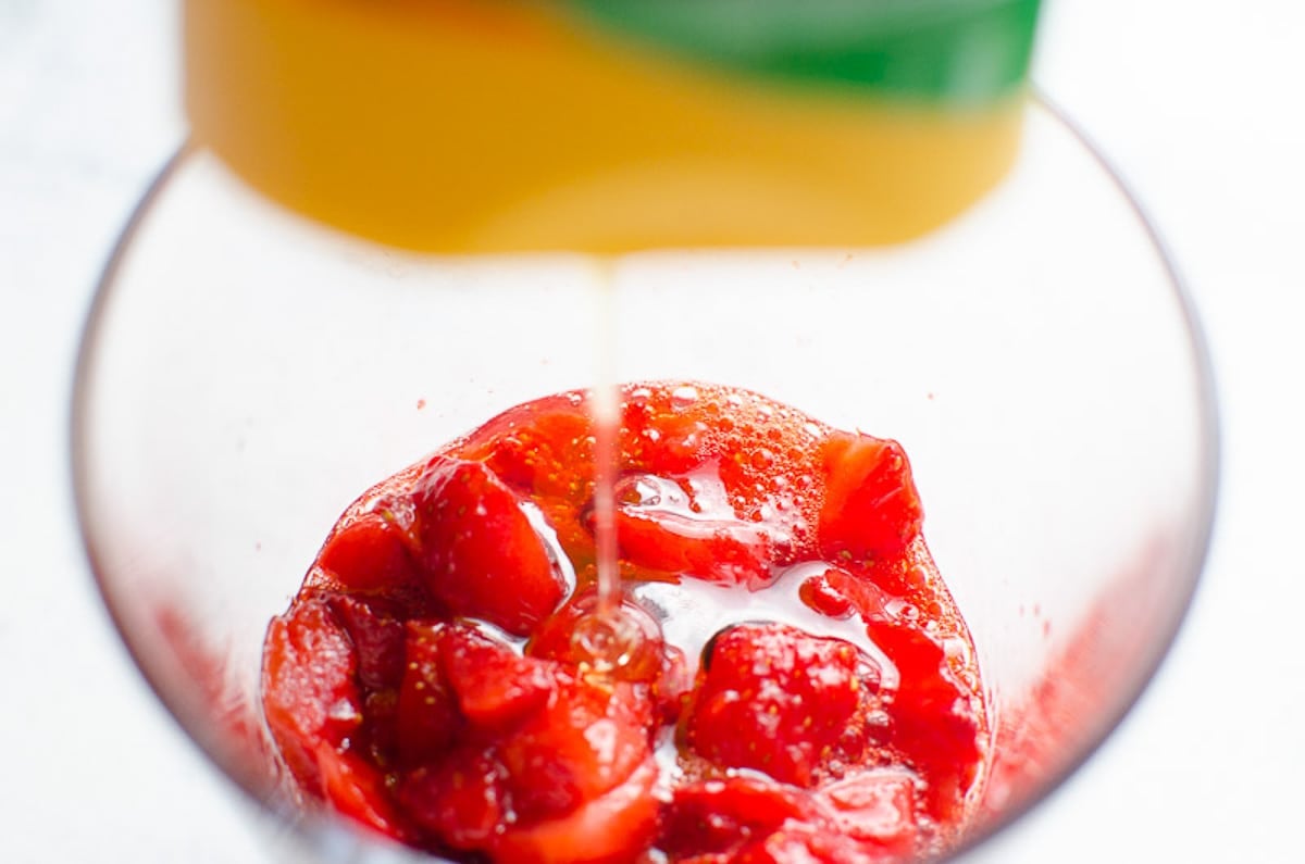 Pouring honey on top of mushy strawberries in a glass.