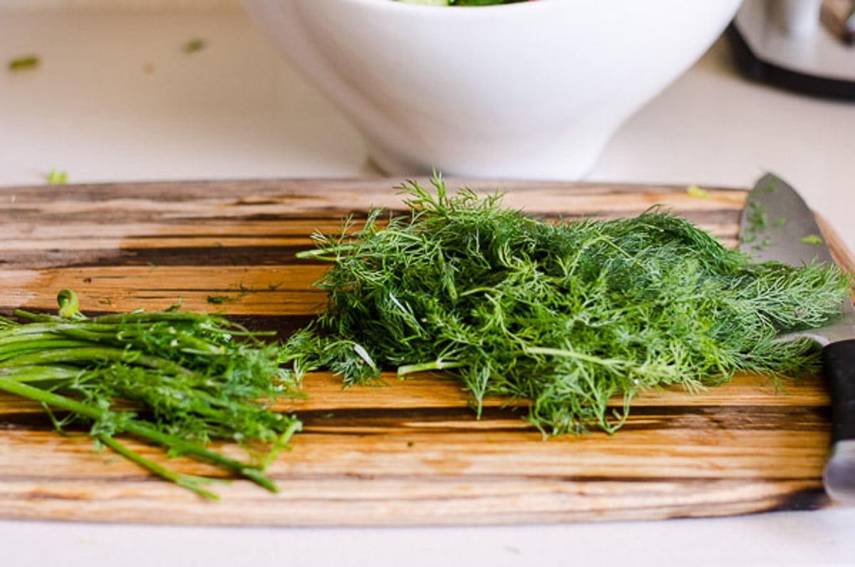 Bunch of fresh dill on cutting board with a knife.