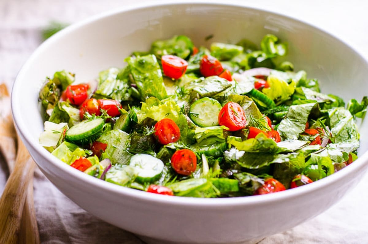 Dressed lettuce salad with tomatoes, cucumbers, and dill in serving bowl.