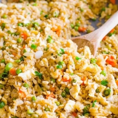 Healthy cauliflower fried rice in skillet with wooden serving spoon.