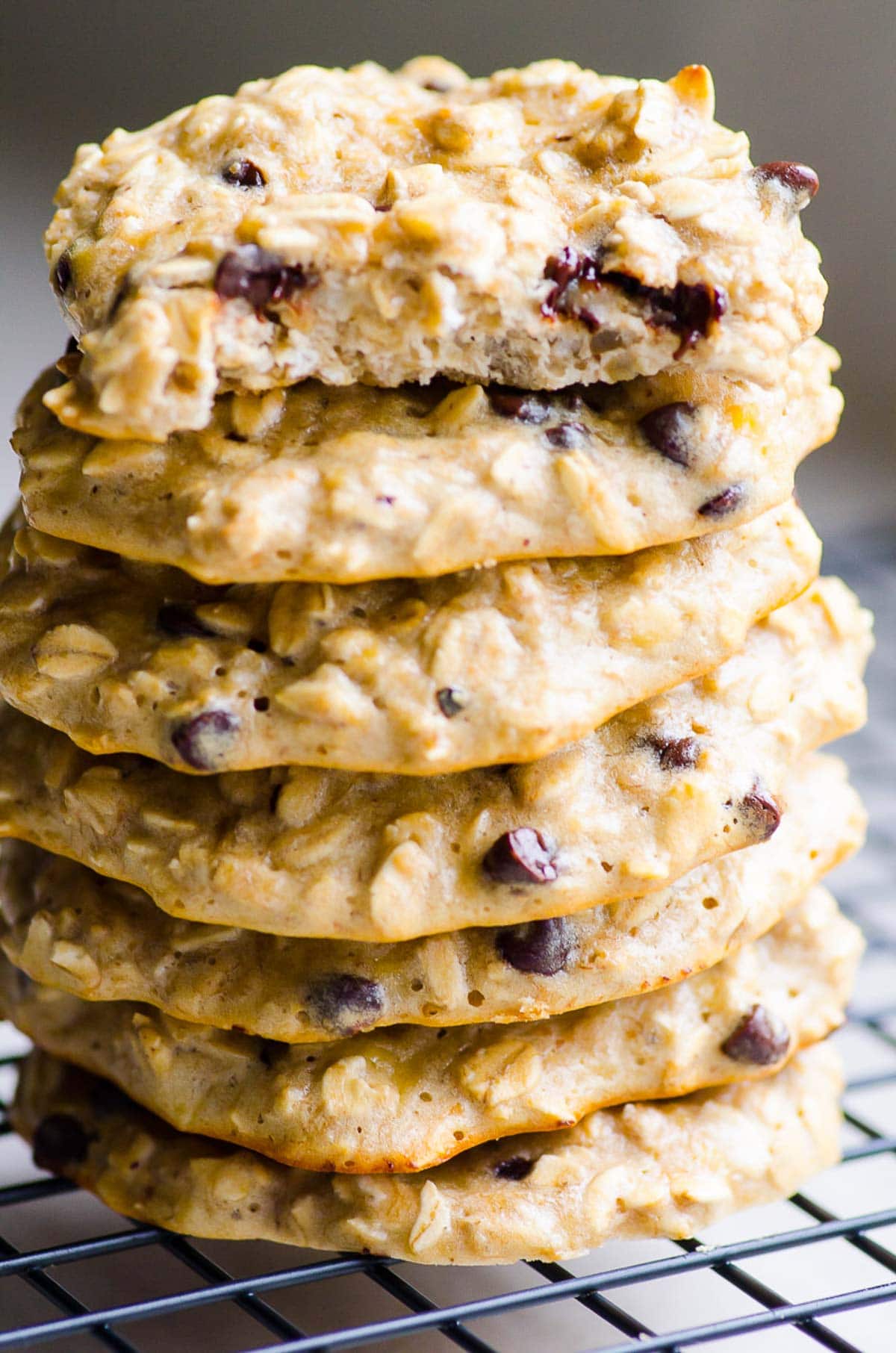 A stack of seven protein cookies with chocolate chips. Top one has a bite taken out showing texture.