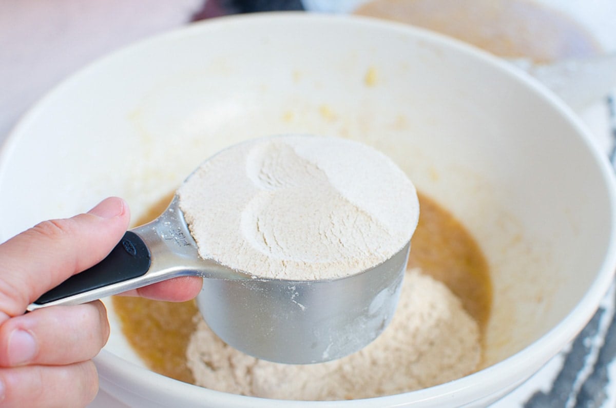 Flour in measuring cup over a bowl with other ingredients.