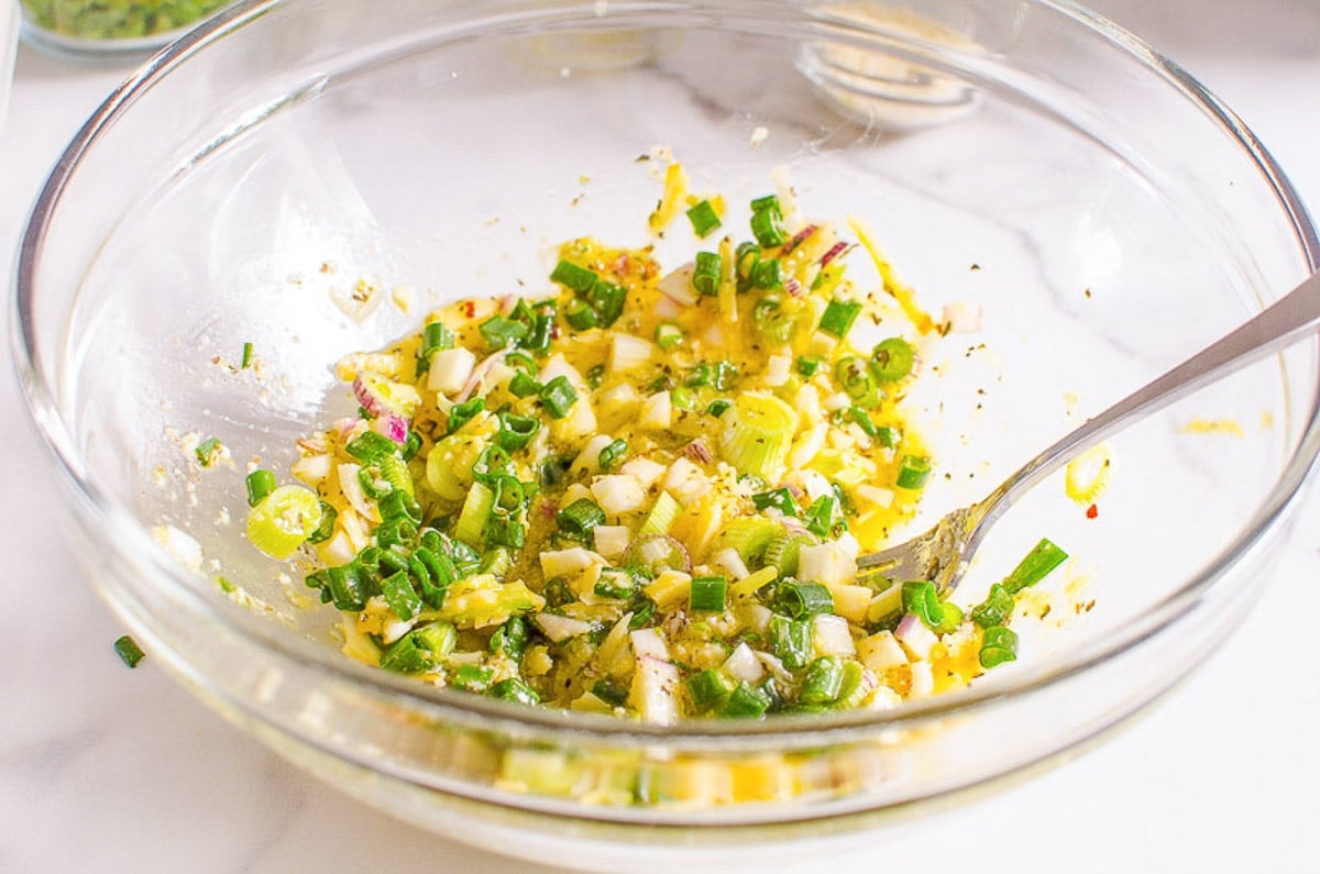 Onion, herbs, eggs and cheese mixed in a bowl with a fork.