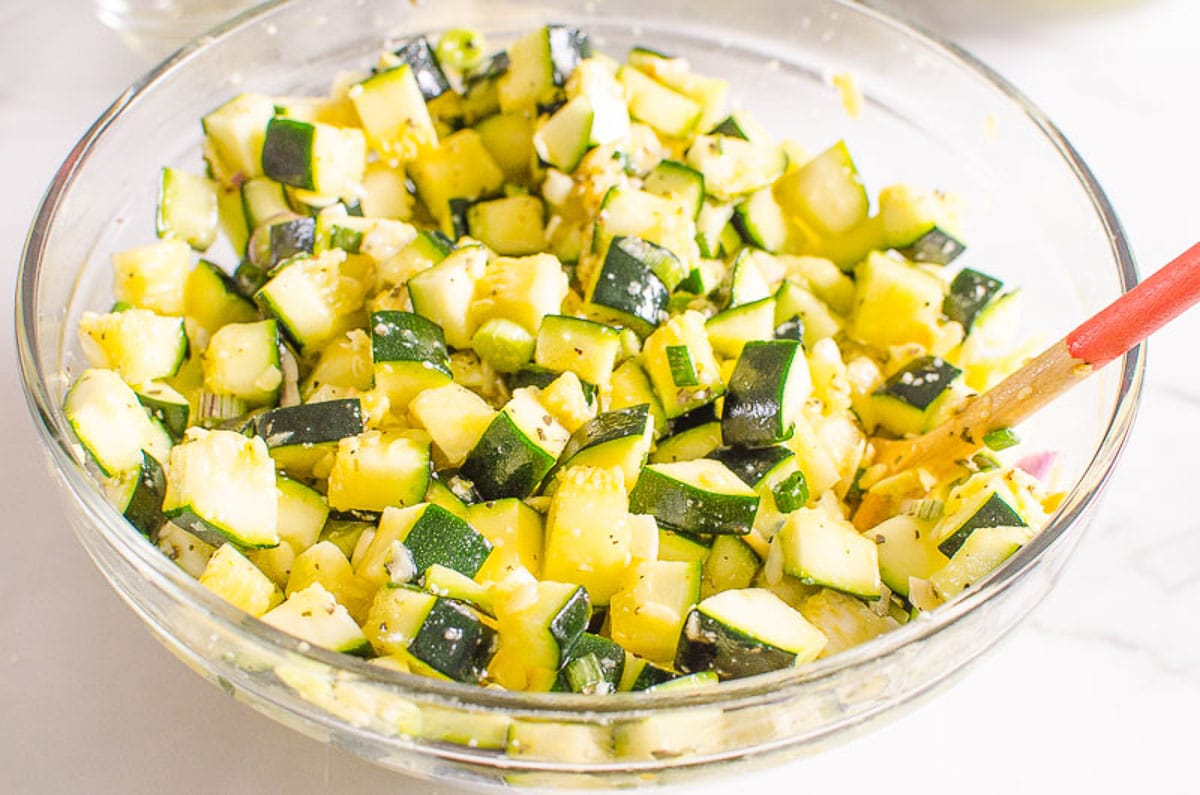 Chopped zucchini being tossed in a bowl with cheese and herb mixture.