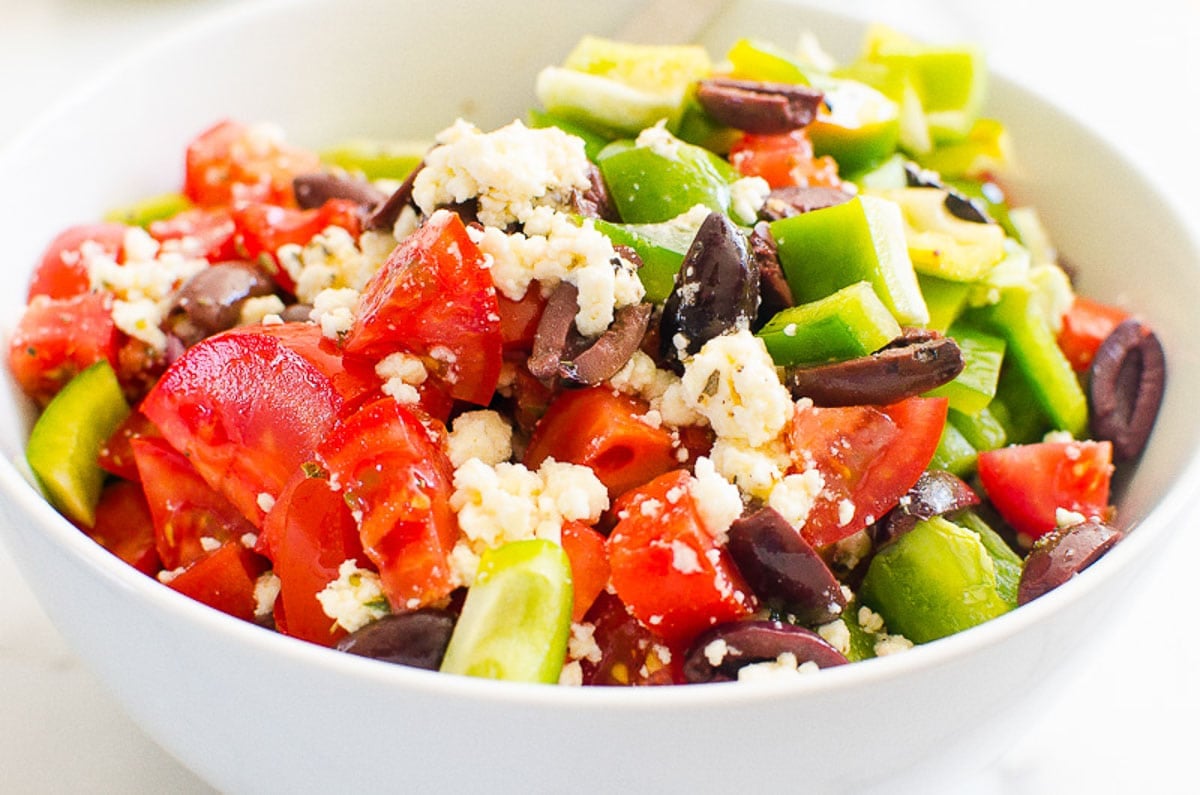 Chopped tomatoes, cucumber, bell pepper, olives with crumbled feta in a bowl.