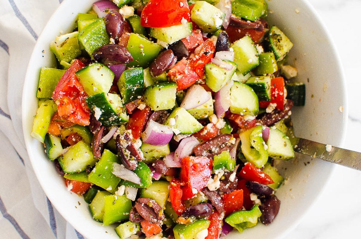 Greek salad in a bowl with spoon and linen napkin nearby.