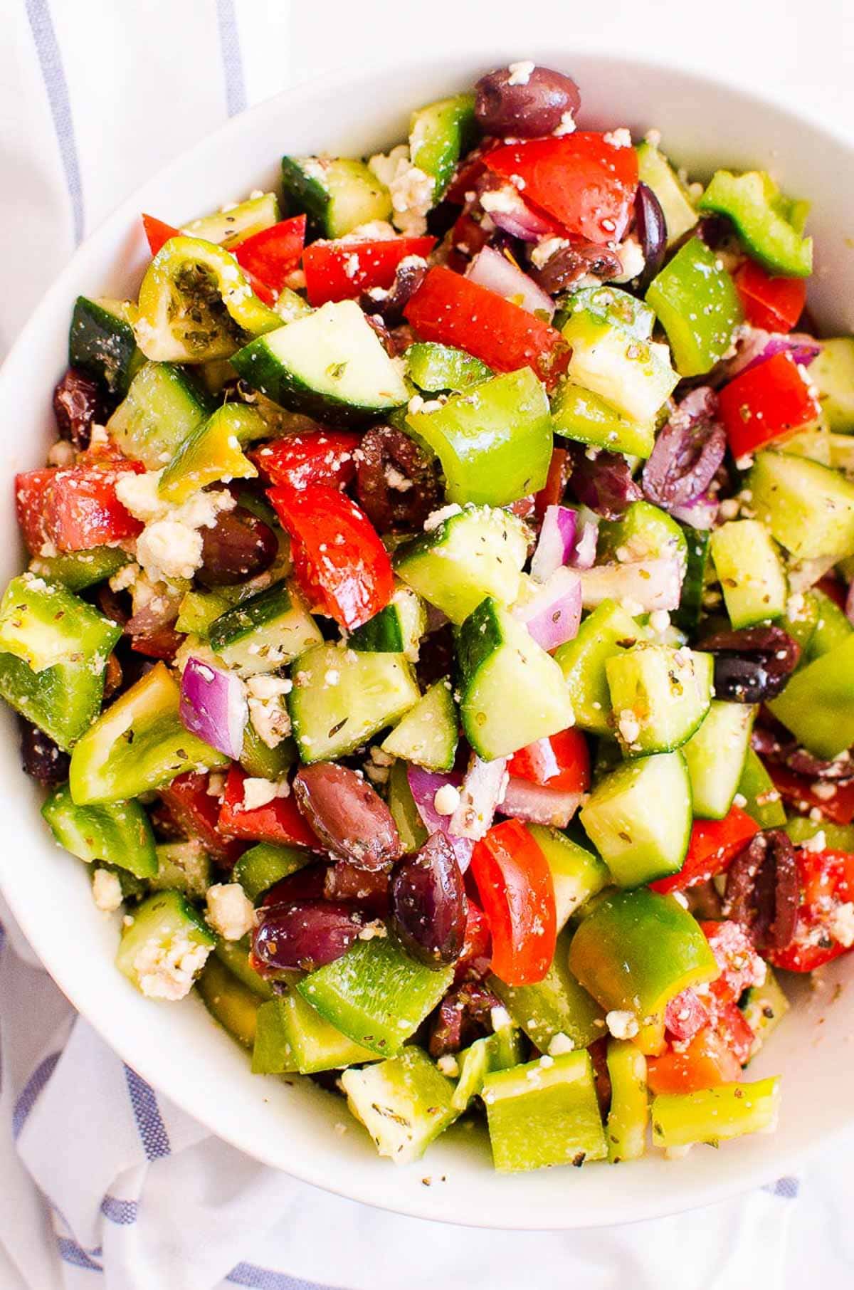 Traditional Greek salad with tomato cucumber, feta, peppers and olives in white bow.